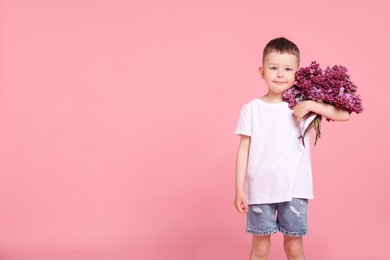 Photo of Little boy with bouquet of lilac flowers on pink background, space for text