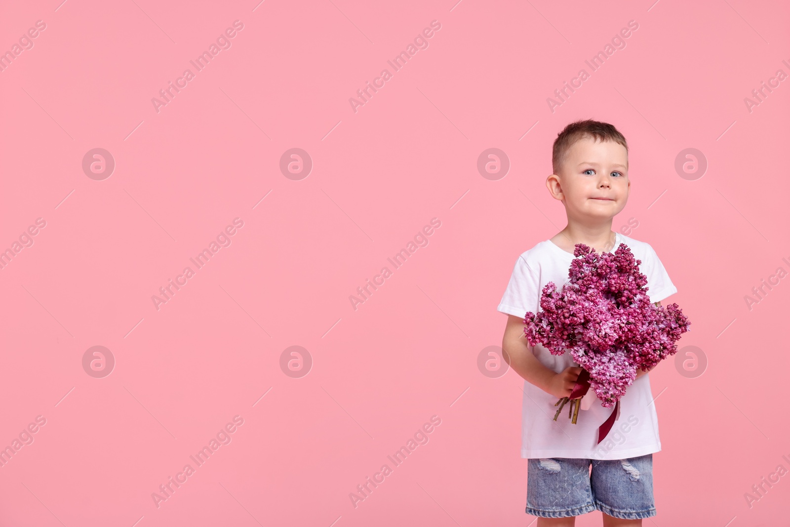 Little boy with bouquet of lilac flowers on pink background, space for text Photo of Little boy with bouquet of lilac flowers on pink background, space for text