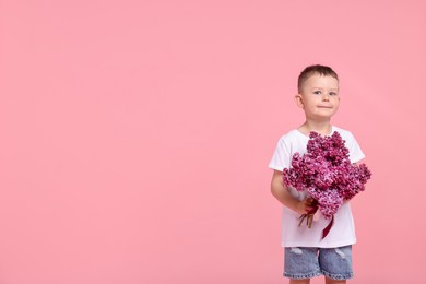 Photo of Little boy with bouquet of lilac flowers on pink background, space for text