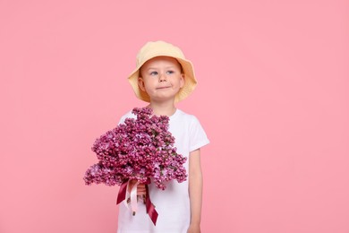 Photo of Little boy with bouquet of lilac flowers on pink background, space for text