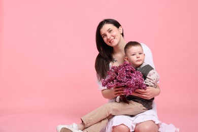 Photo of Mother and her son with bouquet of lilac flowers on pink background, space for text