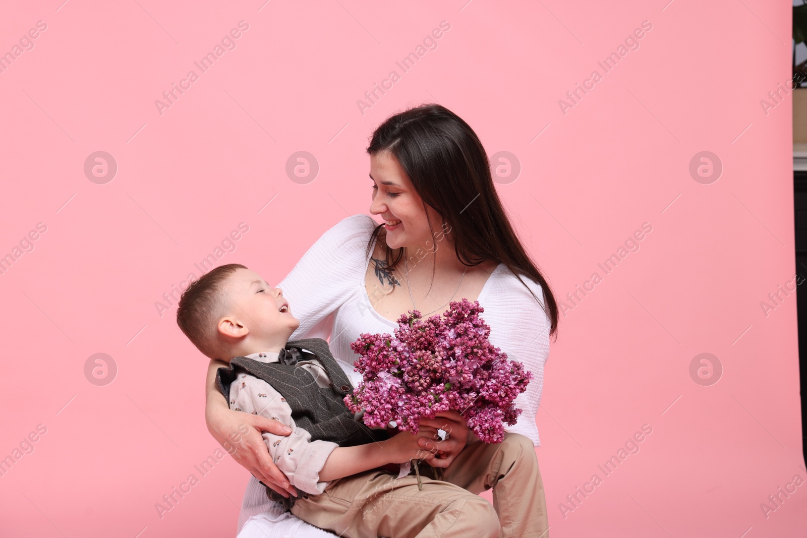 Mother and her son with bouquet of lilac flowers on pink background Photo of Mother and her son with bouquet of lilac flowers on pink background