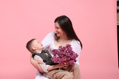 Photo of Mother and her son with bouquet of lilac flowers on pink background