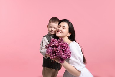 Photo of Mother and her son with bouquet of lilac flowers on pink background