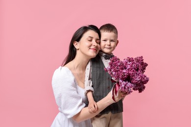 Photo of Mother and her son with bouquet of lilac flowers on pink background
