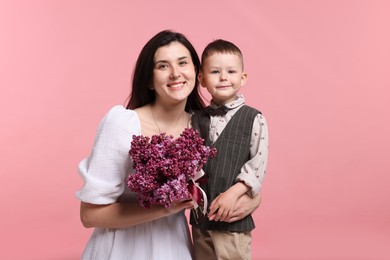 Photo of Mother and her son with bouquet of lilac flowers on pink background