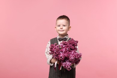 Photo of Little boy with bouquet of lilac flowers on pink background