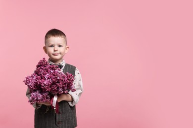 Photo of Little boy with bouquet of lilac flowers on pink background, space for text