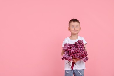 Photo of Little boy with bouquet of lilac flowers on pink background, space for text
