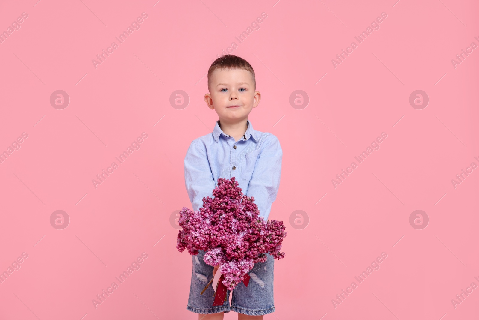 Little boy with bouquet of lilac flowers on pink background Photo of Little boy with bouquet of lilac flowers on pink background