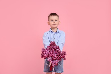Photo of Little boy with bouquet of lilac flowers on pink background