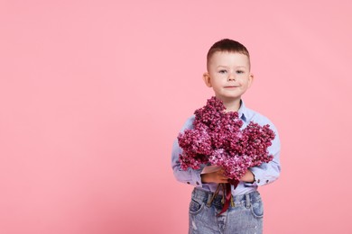 Photo of Little boy with bouquet of lilac flowers on pink background, space for text