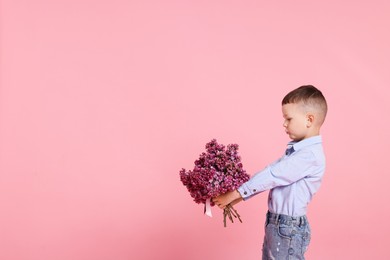 Photo of Little boy with bouquet of lilac flowers on pink background, space for text