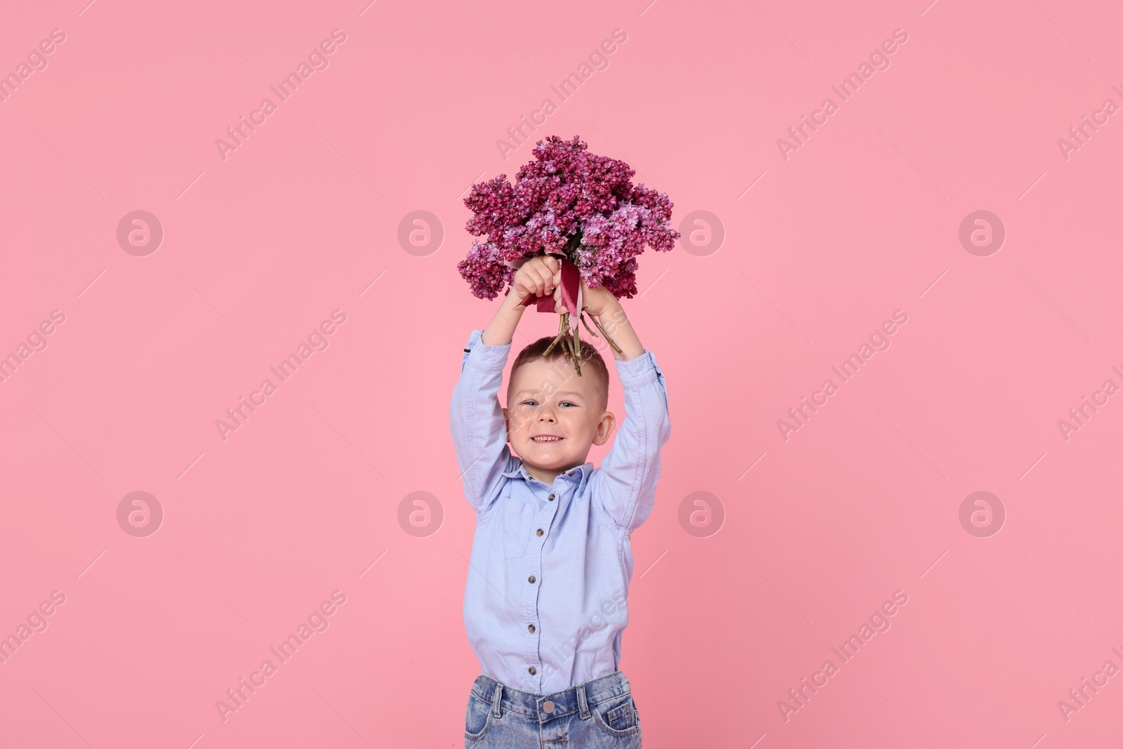 Little boy with bouquet of lilac flowers on pink background Photo of Little boy with bouquet of lilac flowers on pink background