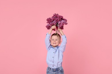 Photo of Little boy with bouquet of lilac flowers on pink background