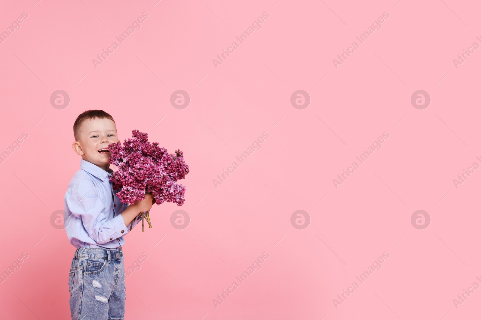 Little boy with bouquet of lilac flowers on pink background, space for text Photo of Little boy with bouquet of lilac flowers on pink background, space for text