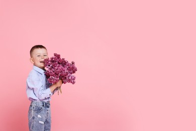 Photo of Little boy with bouquet of lilac flowers on pink background, space for text