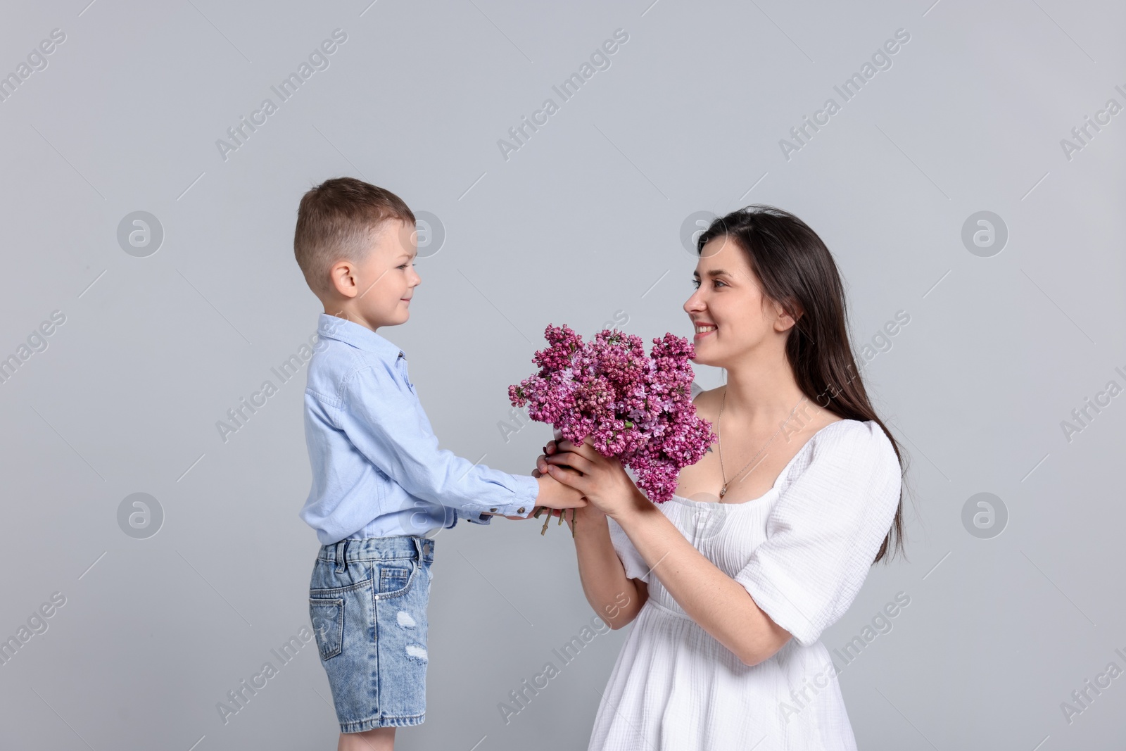 Mother and her son with bouquet of lilac flowers on light grey background Photo of Mother and her son with bouquet of lilac flowers on light grey background