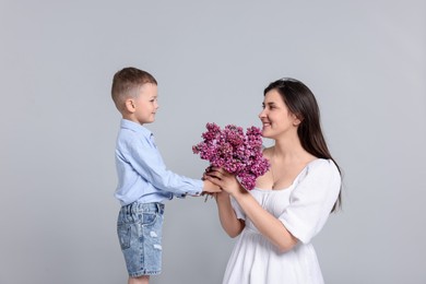 Photo of Mother and her son with bouquet of lilac flowers on light grey background