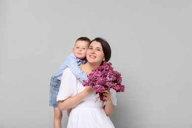 Photo of Mother and her son with bouquet of lilac flowers on light grey background