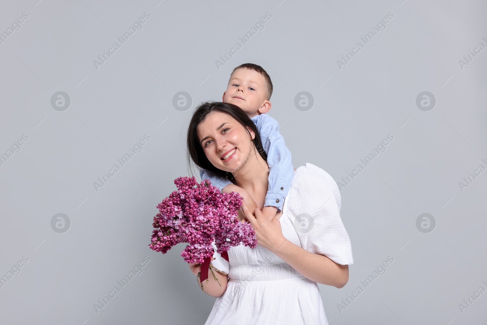 Mother and her son with bouquet of lilac flowers on light grey background Photo of Mother and her son with bouquet of lilac flowers on light grey background