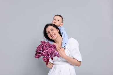 Photo of Mother and her son with bouquet of lilac flowers on light grey background