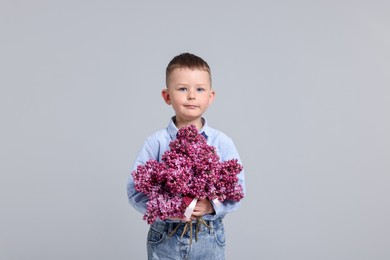 Photo of Little boy with bouquet of lilac flowers on light grey background