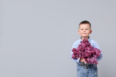 Photo of Little boy with bouquet of lilac flowers on light grey background, space for text