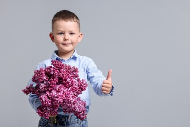 Photo of Little boy with bouquet of lilac flowers showing thumbs up on light grey background, space for text