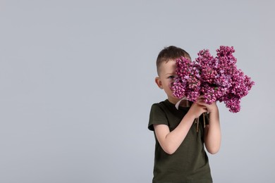 Photo of Little boy with bouquet of lilac flowers on light grey background, space for text