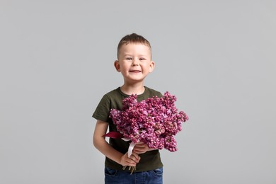 Photo of Little boy with bouquet of lilac flowers on light grey background