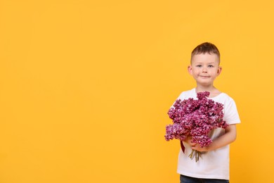 Photo of Little boy with bouquet of lilac flowers on yellow background, space for text