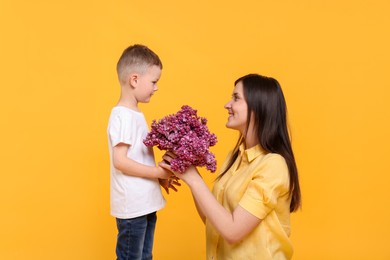 Photo of Mother and her son with bouquet of lilac flowers on yellow background