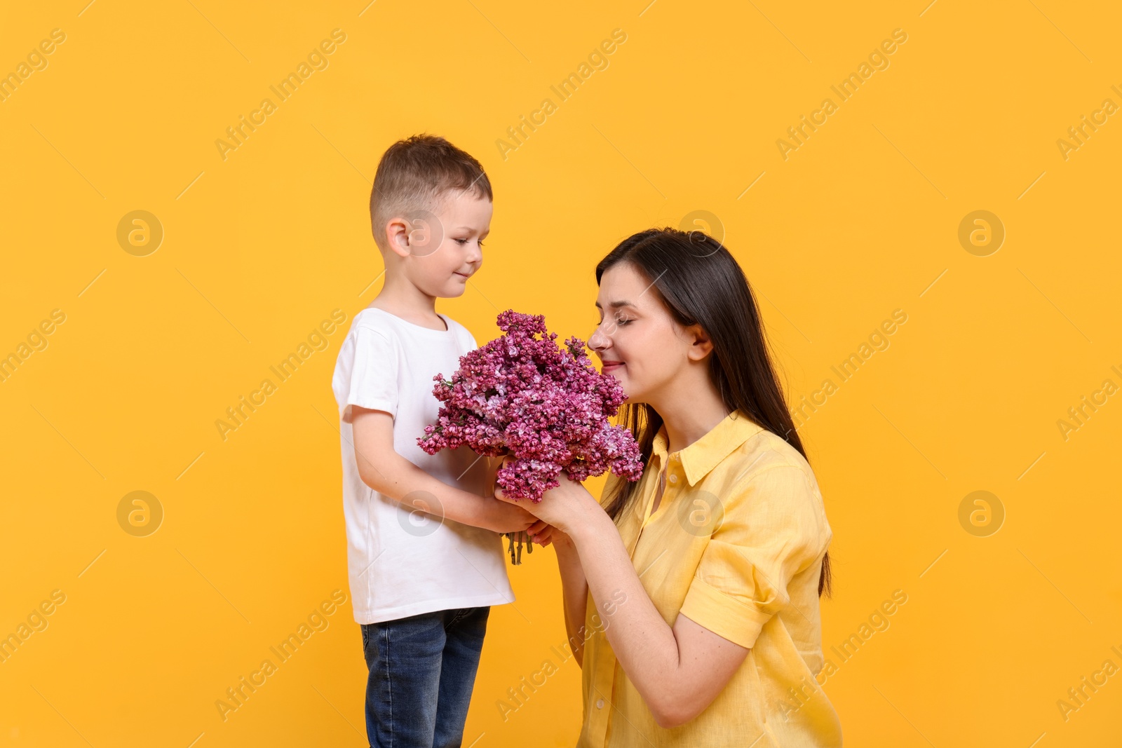 Mother and her son with bouquet of lilac flowers on yellow background Photo of Mother and her son with bouquet of lilac flowers on yellow background