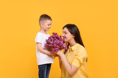 Photo of Mother and her son with bouquet of lilac flowers on yellow background