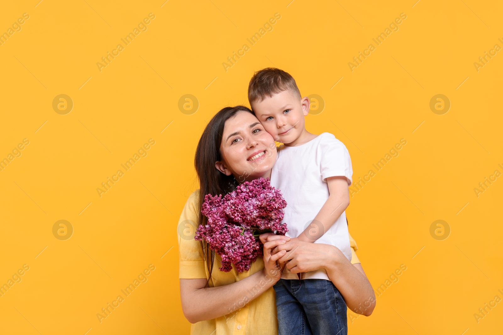 Mother and her son with bouquet of lilac flowers on yellow background Photo of Mother and her son with bouquet of lilac flowers on yellow background