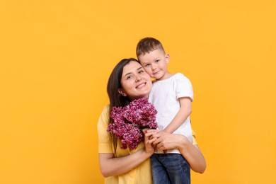Photo of Mother and her son with bouquet of lilac flowers on yellow background