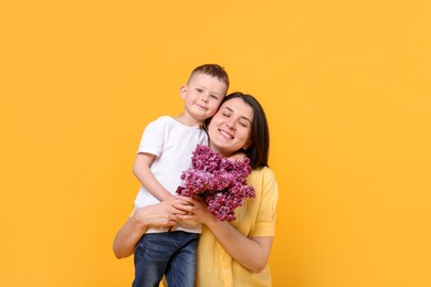 Photo of Mother and her son with bouquet of lilac flowers on yellow background
