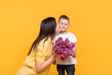Photo of Mother and her son with bouquet of lilac flowers on yellow background