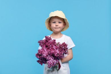 Photo of Little boy with bouquet of lilac flowers on light blue background
