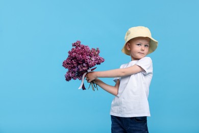 Photo of Little boy with bouquet of lilac flowers on light blue background