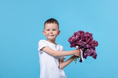 Photo of Little boy with bouquet of lilac flowers on light blue background