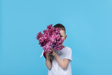Photo of Little boy with bouquet of lilac flowers on light blue background