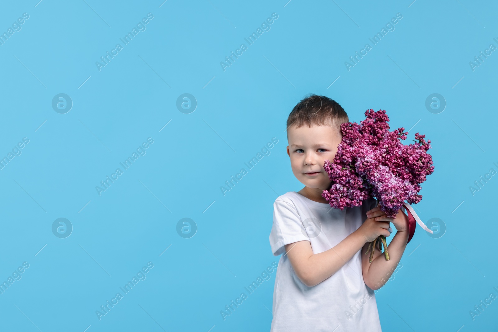 Little boy with bouquet of lilac flowers on light blue background, space for text Photo of Little boy with bouquet of lilac flowers on light blue background, space for text