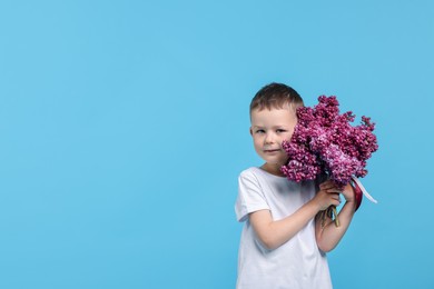 Photo of Little boy with bouquet of lilac flowers on light blue background, space for text