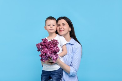 Photo of Mother and her son with bouquet of lilac flowers on light blue background