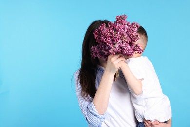 Photo of Mother and her son with bouquet of lilac flowers on light blue background, space for text