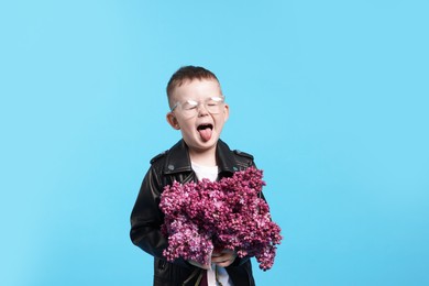 Photo of Little boy with bouquet of lilac flowers on light blue background