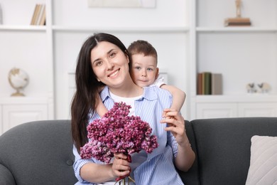 Photo of Mother and her son with bouquet of lilac flowers at home