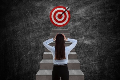 Image of Targeting, goal achievement. Business woman walking up stairs leading to bullseye with arrow